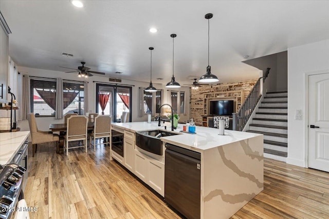 kitchen featuring sink, decorative light fixtures, black dishwasher, an island with sink, and white cabinets