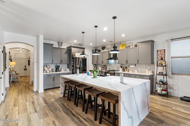 kitchen featuring gray cabinets, stainless steel appliances, a kitchen bar, decorative light fixtures, and a large island with sink