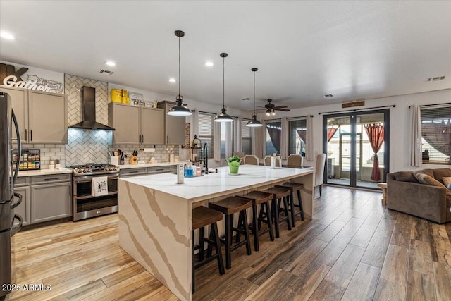 kitchen with a breakfast bar, hanging light fixtures, a center island with sink, appliances with stainless steel finishes, and wall chimney range hood