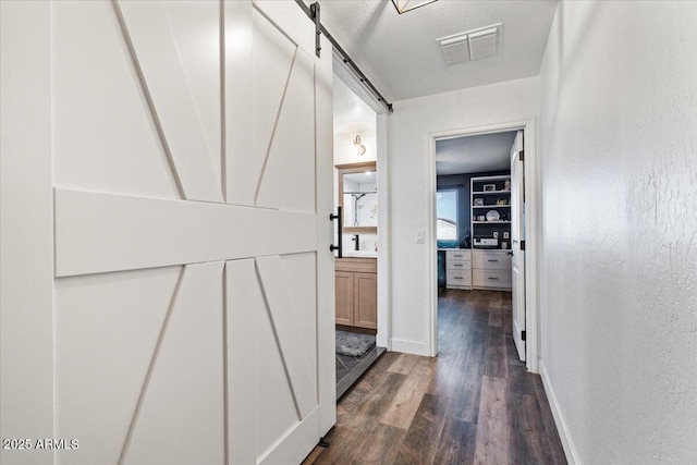 hall with dark hardwood / wood-style flooring, a barn door, and a textured ceiling