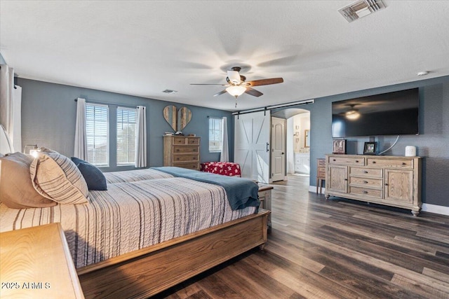 bedroom featuring ceiling fan, ensuite bathroom, a textured ceiling, dark hardwood / wood-style flooring, and a barn door