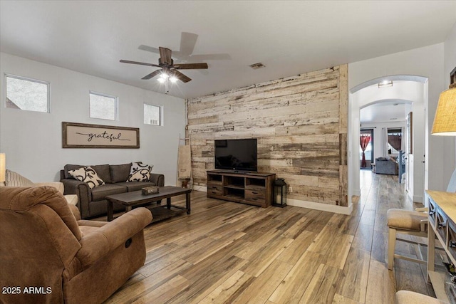 living room with a healthy amount of sunlight, hardwood / wood-style floors, ceiling fan, and wood walls