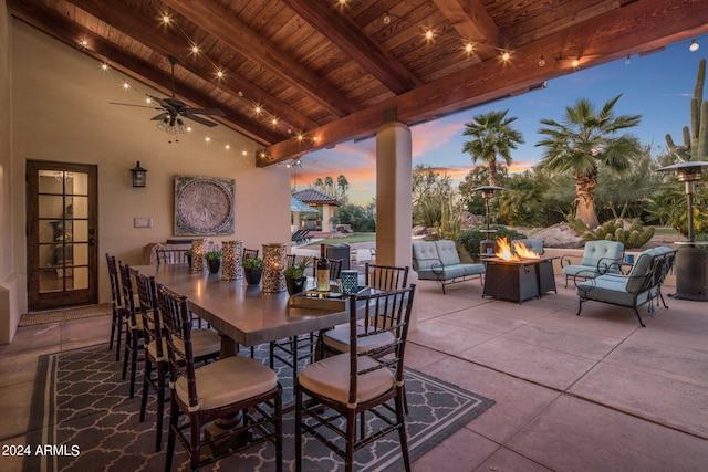 patio terrace at dusk featuring outdoor dining area, an outdoor fire pit, and ceiling fan