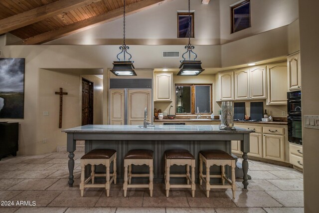 kitchen featuring decorative light fixtures, cream cabinetry, high vaulted ceiling, and a breakfast bar