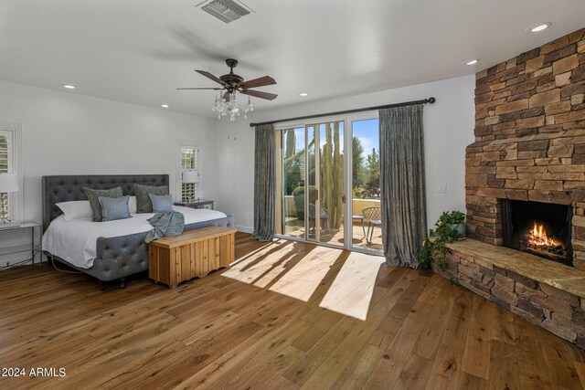 bedroom featuring ceiling fan, a stone fireplace, hardwood / wood-style flooring, and access to exterior