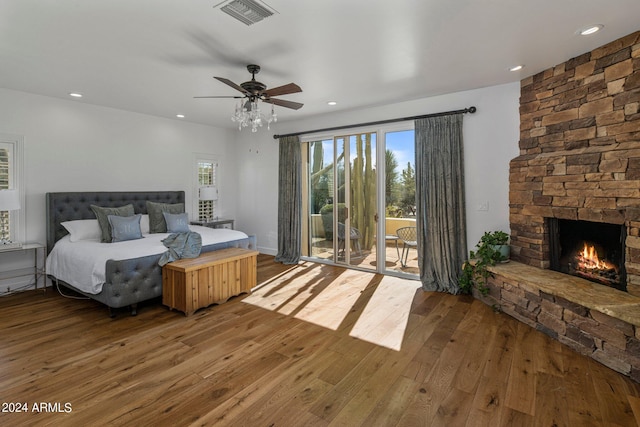 bedroom featuring a ceiling fan, a stone fireplace, visible vents, access to exterior, and wood-type flooring