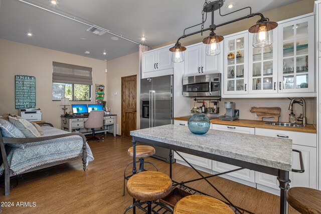 kitchen with pendant lighting, white cabinetry, appliances with stainless steel finishes, light wood-type flooring, and wood counters