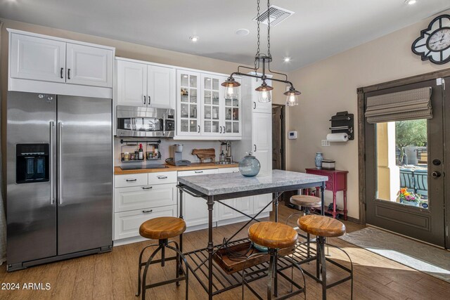 kitchen featuring appliances with stainless steel finishes, decorative backsplash, white cabinetry, light hardwood / wood-style flooring, and decorative light fixtures