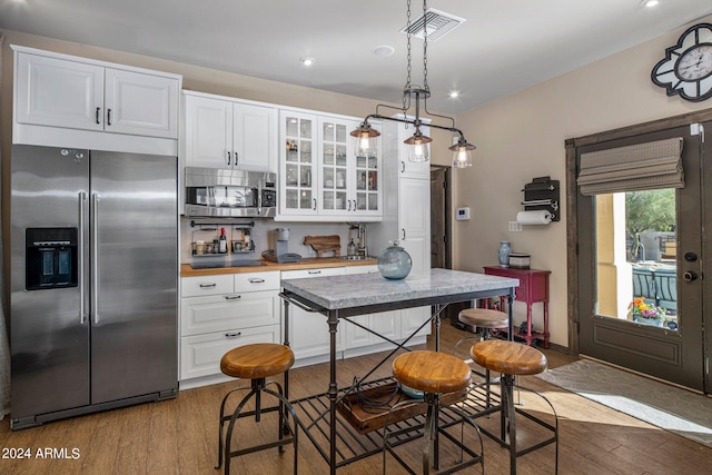 kitchen featuring visible vents, white cabinets, glass insert cabinets, appliances with stainless steel finishes, and wood finished floors
