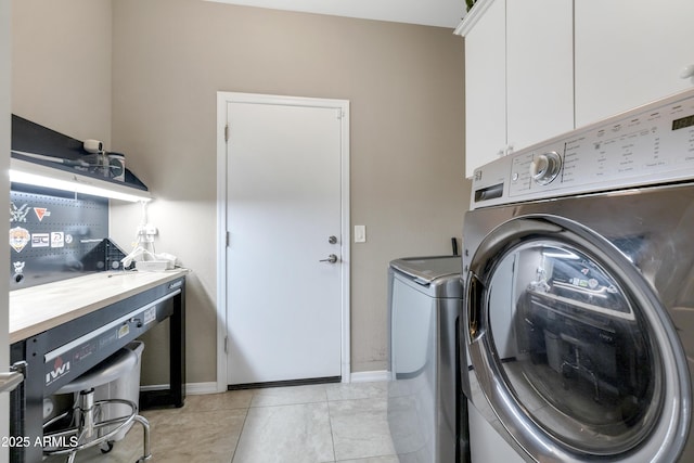 clothes washing area featuring cabinets, washing machine and dryer, and light tile patterned floors