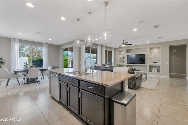 kitchen featuring sink, hanging light fixtures, light stone countertops, an island with sink, and built in shelves