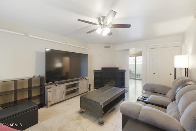 living room featuring ceiling fan, a fireplace, and light tile patterned flooring