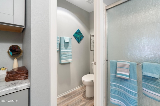 full bathroom with visible vents, toilet, a shower with door, wood finished floors, and baseboards