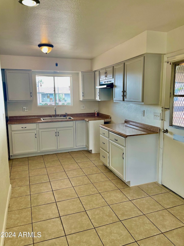 kitchen with wood counters, light tile patterned floors, a textured ceiling, and sink