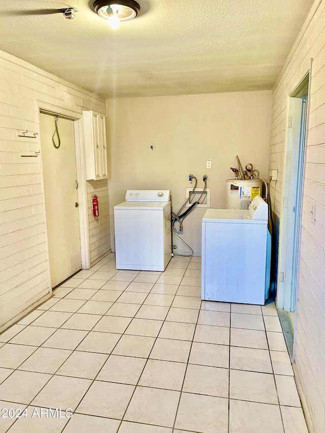 clothes washing area with electric water heater, a textured ceiling, and brick wall