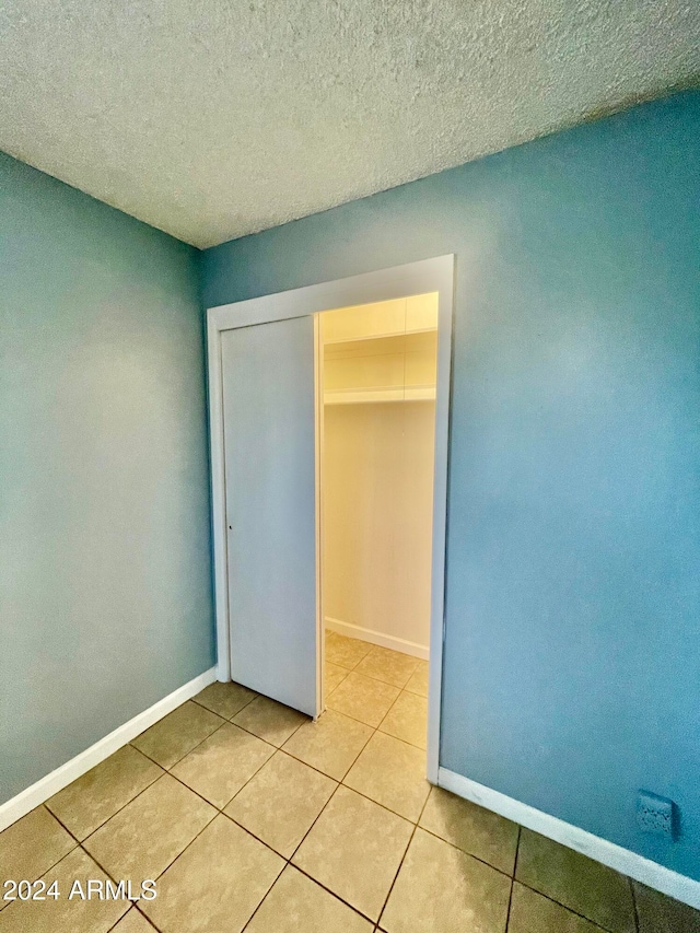 unfurnished bedroom featuring a closet, light tile patterned floors, and a textured ceiling