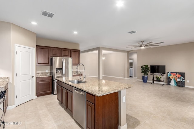 kitchen featuring a center island with sink, sink, ceiling fan, light stone countertops, and appliances with stainless steel finishes