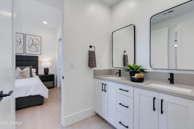 ensuite bathroom featuring wood finished floors, a sink, visible vents, and baseboards