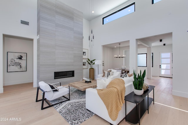 living room featuring a notable chandelier, a fireplace, light wood finished floors, a towering ceiling, and baseboards