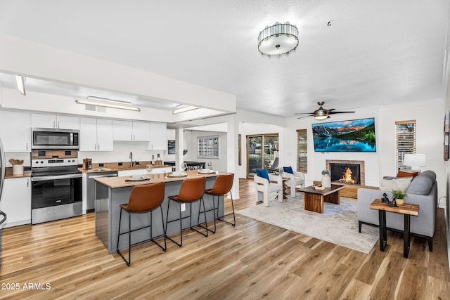 7832 E Via Marina, Scottsdale, AZ 85258 - kitchen with stainless steel appliances, light wood-type flooring, a kitchen breakfast bar, a brick fireplace, and open floor plan