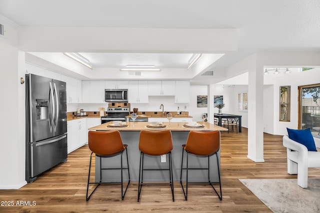 7832 E Via Marina, Scottsdale, AZ 85258 - kitchen with stainless steel appliances, a tray ceiling, light wood-type flooring, white cabinetry, and a kitchen bar