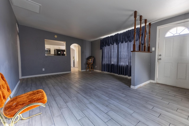 entryway featuring arched walkways, wood finished floors, and baseboards