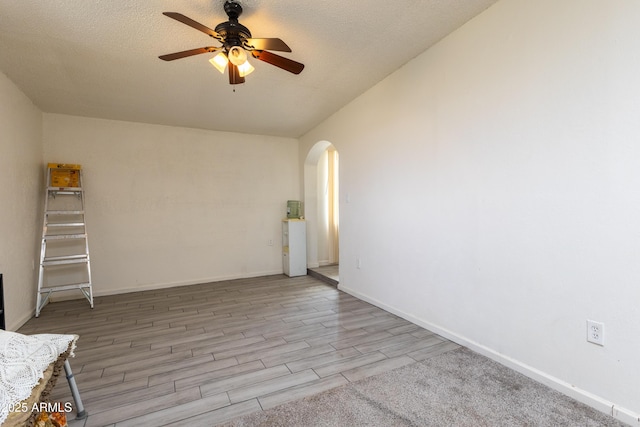 spare room with arched walkways, a textured ceiling, baseboards, and wood finished floors