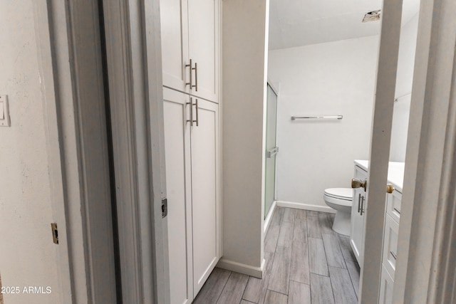 bathroom with toilet, wood finish floors, vanity, baseboards, and a shower stall