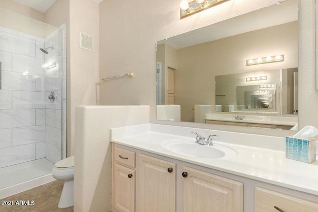 full bath featuring visible vents, toilet, tiled shower, and vanity