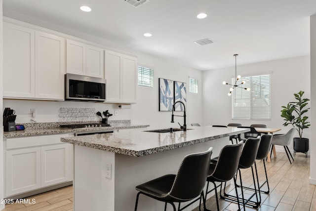 23037 E Domingo Rd, Queen Creek, AZ 85142 - kitchen with stainless steel appliances, a sink, light stone counters, white cabinets, and an island with sink