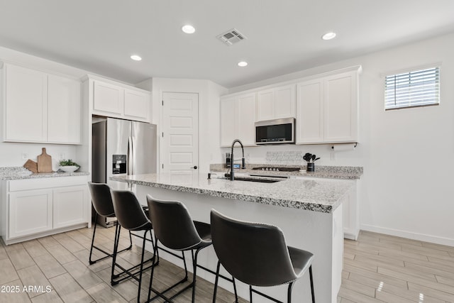 23037 E Domingo Rd, Queen Creek, AZ 85142 - kitchen with stainless steel appliances, a sink, white cabinets, wood tiled floors, and a kitchen breakfast bar