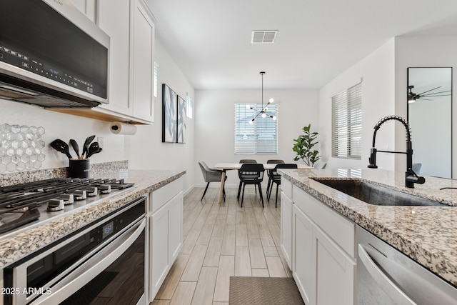 23037 E Domingo Rd, Queen Creek, AZ 85142 - kitchen with stainless steel appliances, a sink, white cabinets, wood finish floors, and a chandelier