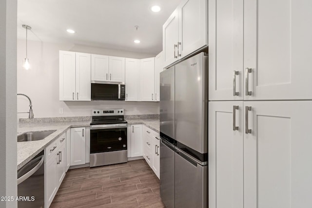kitchen featuring white cabinets, stainless steel appliances, light stone countertops, and a sink