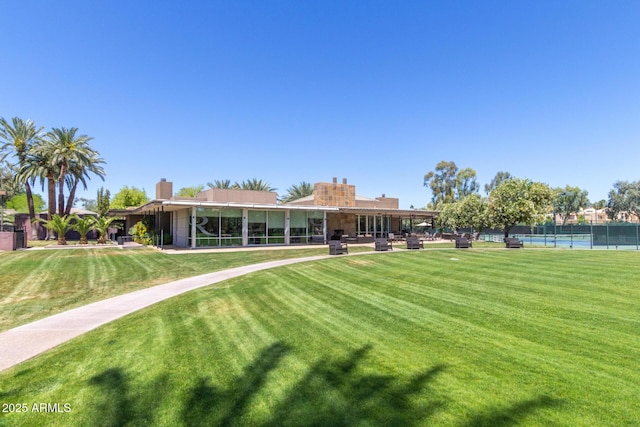 rear view of house featuring a lawn, a tennis court, fence, and a chimney