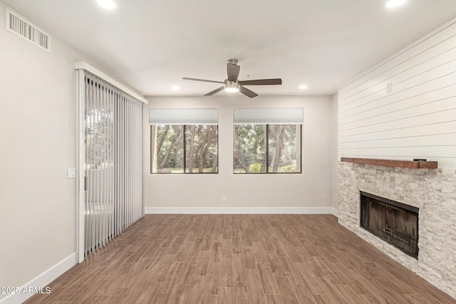 unfurnished living room with visible vents, wood finished floors, baseboards, a stone fireplace, and a ceiling fan