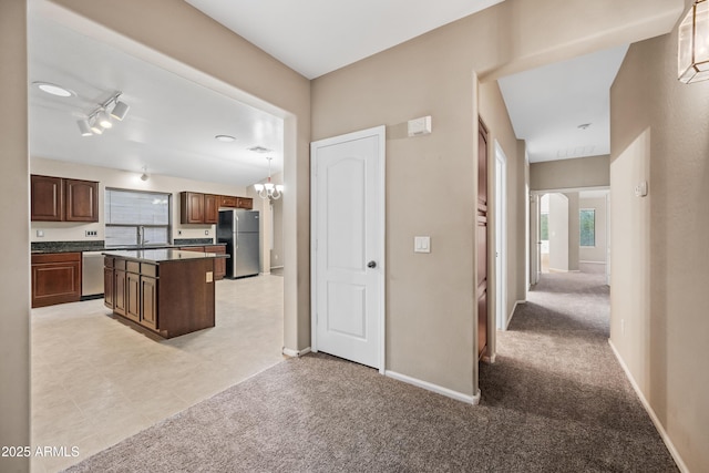 kitchen with a kitchen island, hanging light fixtures, light colored carpet, a notable chandelier, and stainless steel appliances