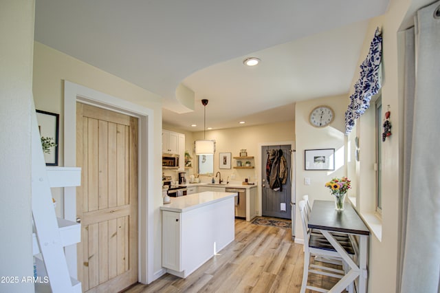 kitchen featuring pendant lighting, appliances with stainless steel finishes, white cabinetry, light hardwood / wood-style floors, and sink