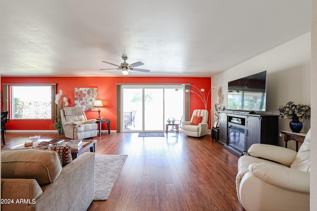 living room featuring a fireplace, ceiling fan, plenty of natural light, and dark wood-type flooring