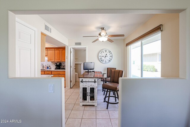 kitchen featuring decorative backsplash, light tile patterned flooring, kitchen peninsula, a kitchen bar, and ceiling fan