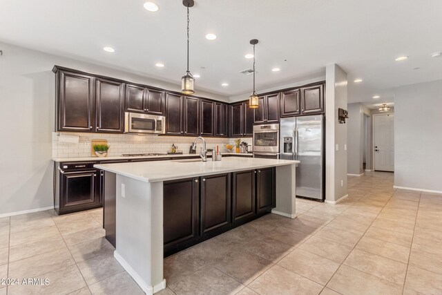 kitchen featuring pendant lighting, appliances with stainless steel finishes, a kitchen island with sink, sink, and dark brown cabinetry