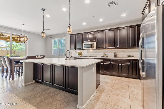 kitchen with a kitchen island with sink, tasteful backsplash, light tile patterned floors, stainless steel appliances, and hanging light fixtures