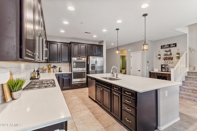 kitchen featuring a kitchen island with sink, sink, hanging light fixtures, appliances with stainless steel finishes, and dark brown cabinetry