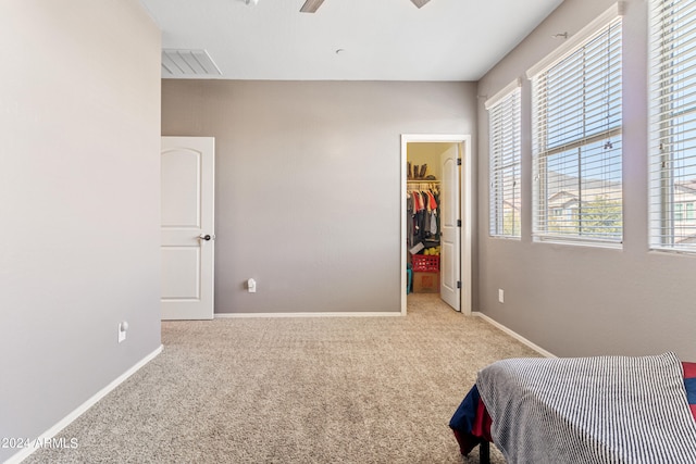 bedroom featuring light colored carpet, a walk in closet, ceiling fan, and a closet