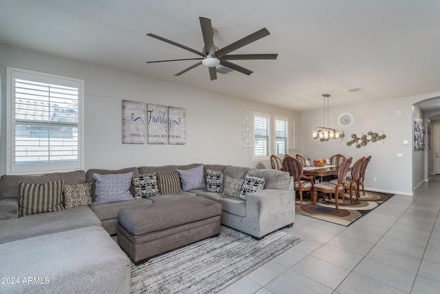 tiled living room with ceiling fan with notable chandelier