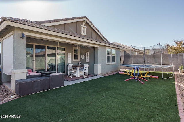 rear view of property featuring a lawn, a patio, and a trampoline