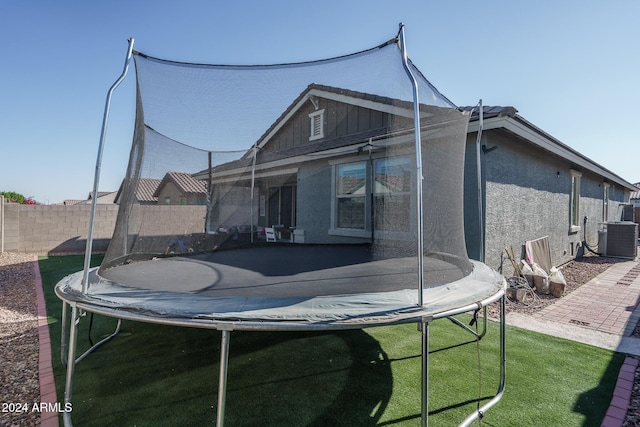 back of property featuring a trampoline, a yard, and central AC