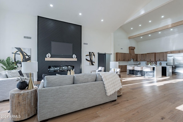 living room with a barn door, light hardwood / wood-style flooring, and high vaulted ceiling