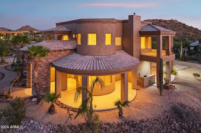 back house at dusk with a mountain view and a balcony