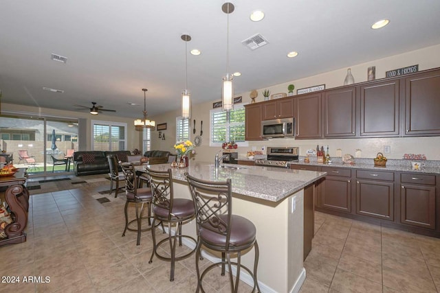 kitchen featuring light stone counters, a kitchen breakfast bar, a center island with sink, appliances with stainless steel finishes, and ceiling fan