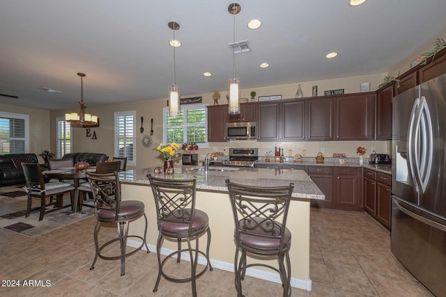 kitchen with hanging light fixtures, a center island with sink, stainless steel appliances, and a breakfast bar